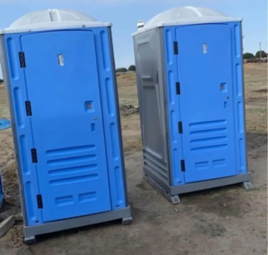 Two standard blue porta potties set on level ground at a dirt jobsite