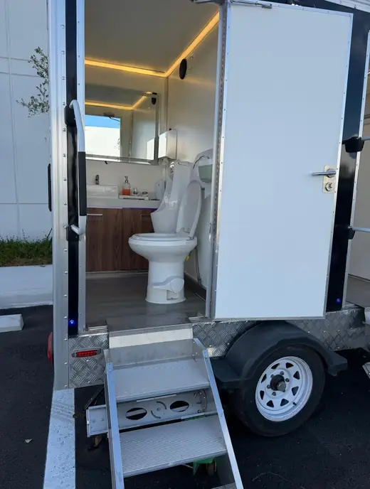 Restroom trailer entry steps with handrail and an open stall door