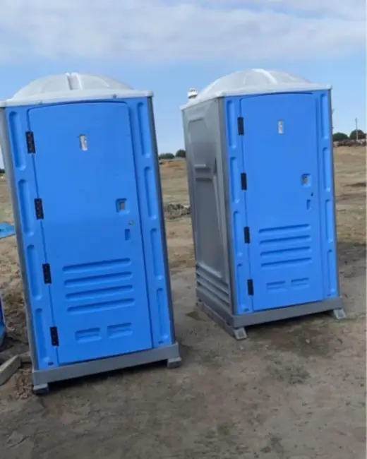 Two standard porta potties on a level dirt jobsite
