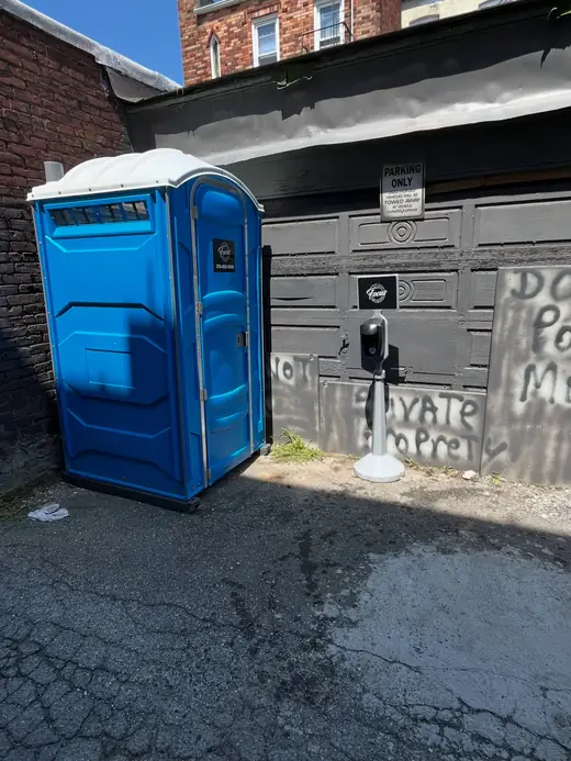 Blue standard porta potty placed beside a building on a paved jobsite